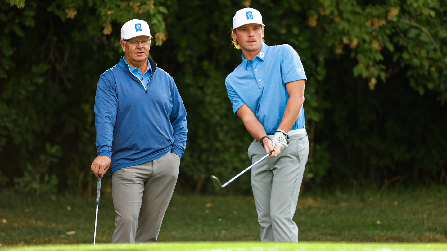 BYU golf coach Bruce Brockbank watches as Carson Lundell hits a golf shot.