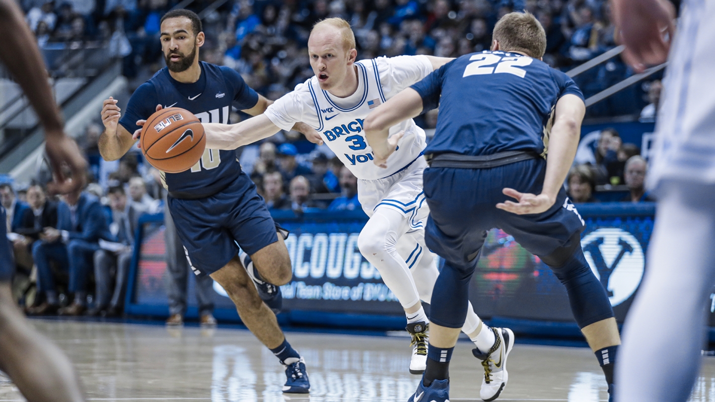 TJ Haws dribbles the basketball between two Oral Roberts players in the Marriott Center.